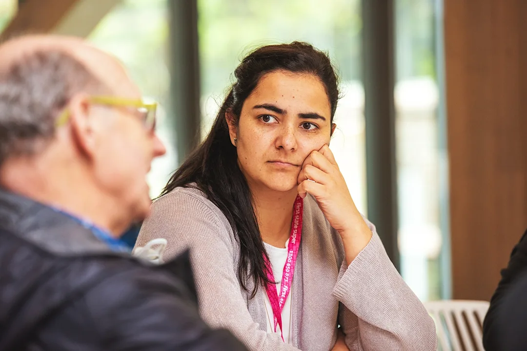 A photo of two participants in a workshop. The person closest to the camera is looking to the right and speaking. Another person is in the centre of the frame, listening intently.