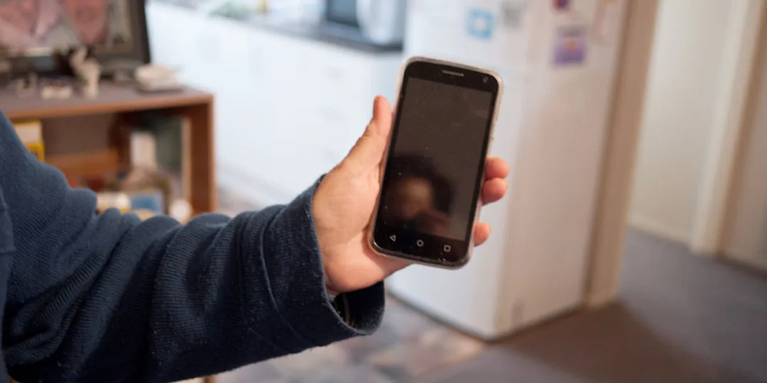 A research participant holds out their mobile phone, the screen is off. They are in their home. 