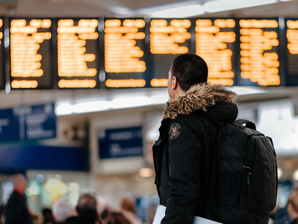 Photo of a man at an airport looking at departure and arrival times on screens. 