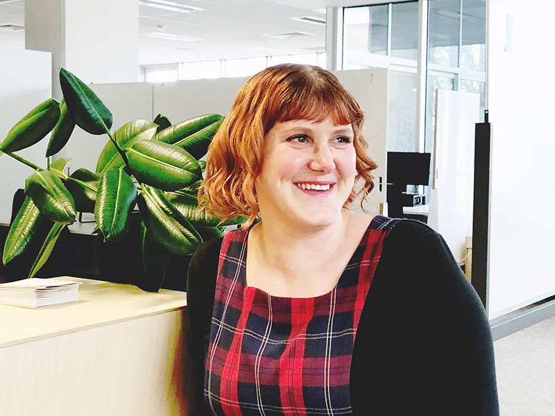 A photo of Rebecca LeSeouf in the Paper Giant Studio. It's a bright day and there's a plant and whiteboards in the background.