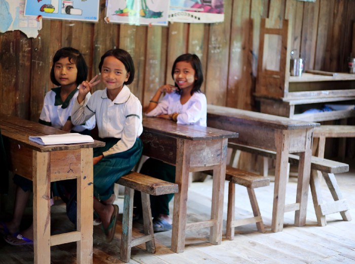 Three female primary school students smiling at school in Chin State.
