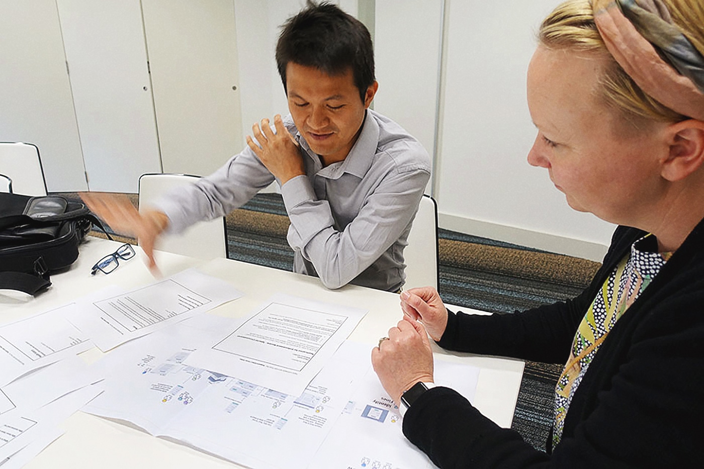 A photo of two people sitting at a table reviewing some printed documents. There is a user flow diagram printed, which outlines the key steps someone takes within a fines journey.