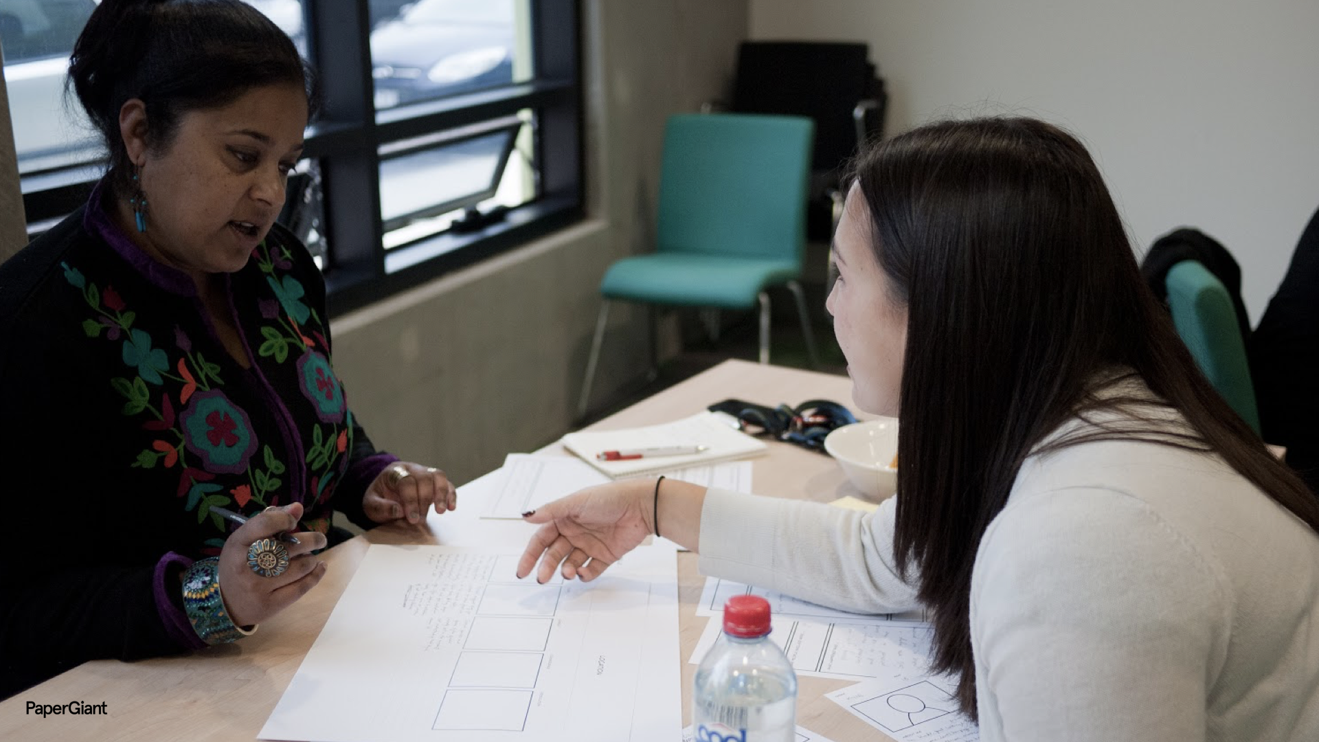 A researcher discusses a piece of paper with a young person at a table
