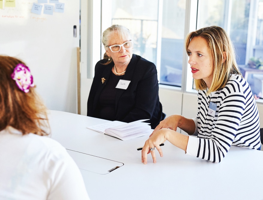 A photo from a workshop run with GMCT. There is a group of three people sitting around a table having a conversation with each other.