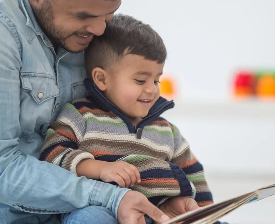A father and son sitting together and reading a book.