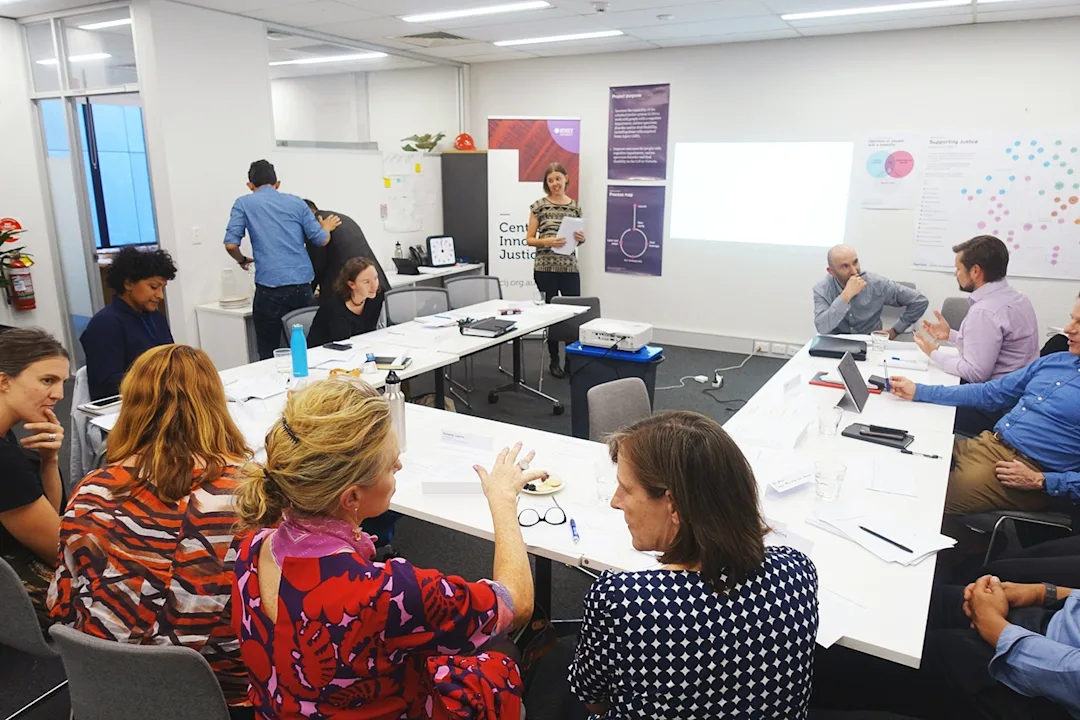 Workshop participants around a large table, having discussions in small groups. 