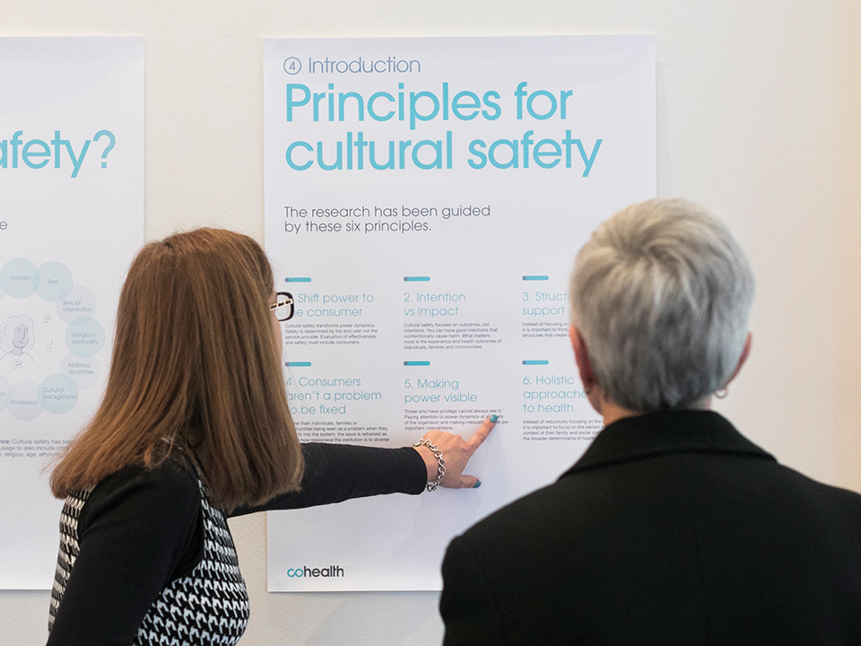 Two people standing next to a poster that shows 6 principles for cultural safety.