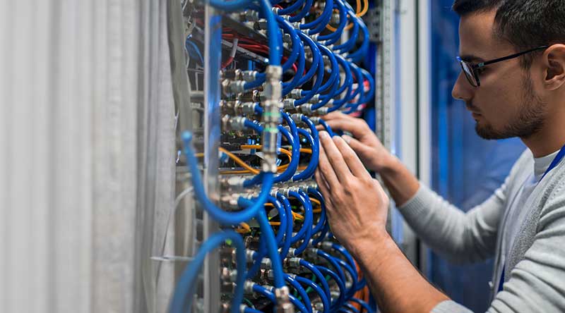 man connecting wires in server cabinet while working with supercomputer in data center