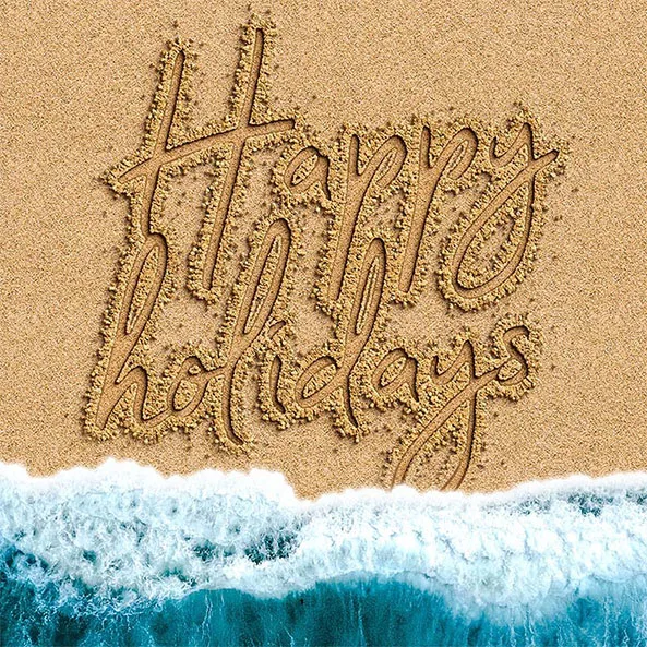 Image of Happy holidays written into sand at a beach with tide coming in