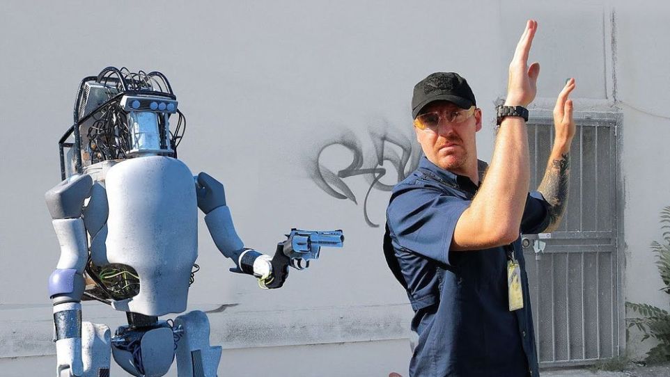 A robot points a gun at a human.