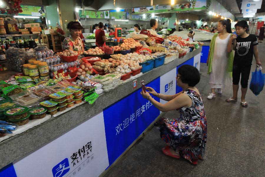 A woman crouches and scans a QR code in front of a stand selling fruits and vegetables.