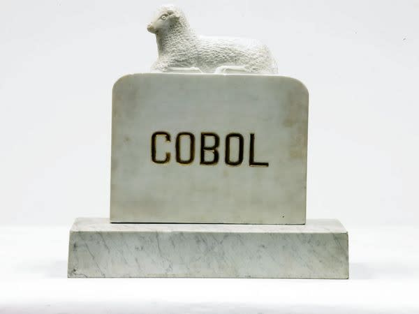 A granite tombstone with a sheep on top, that reads COBOL.