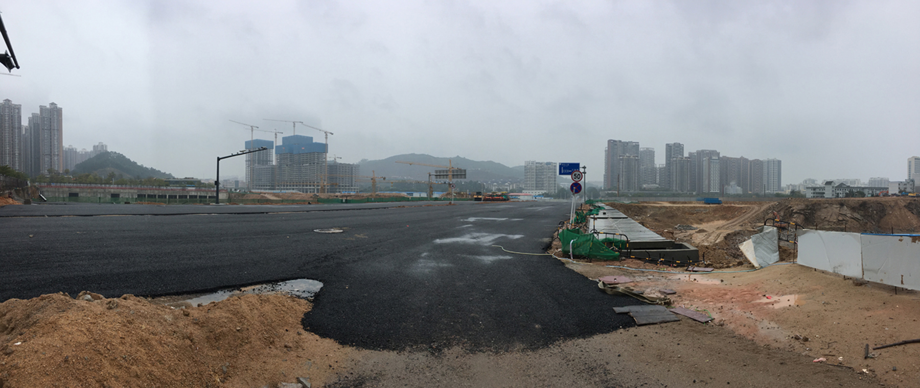 An overcast urban landscape with concrete in the foreground and cranes over tall buildings in the background.