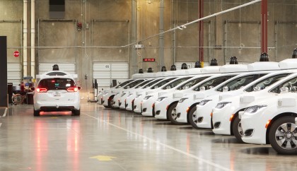 A white, Waymo Pacifica minivan leaving the depot full of other Waymo vehicles