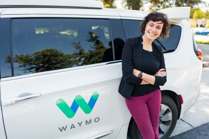 A photo of Anca Dragan in front of a white, Waymo Pacifica minivan 