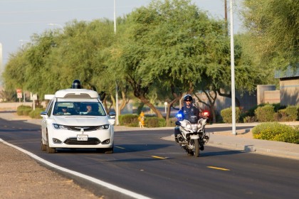 A photo of a white, Waymo Pacifica minivan yielding to a motorcycle police in Arizona