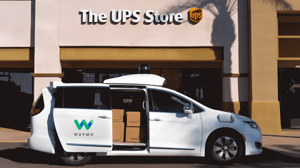 A gif of brown boxes shuffling positions inside of a white, Waymo Pacifica minivan in front of a UPS store