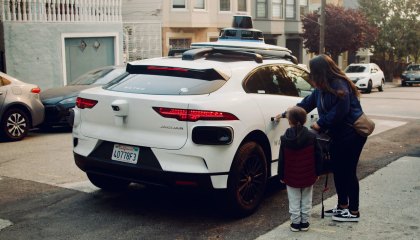 A parent and their child opening the door to a white, Waymo vehicle in San Francisco