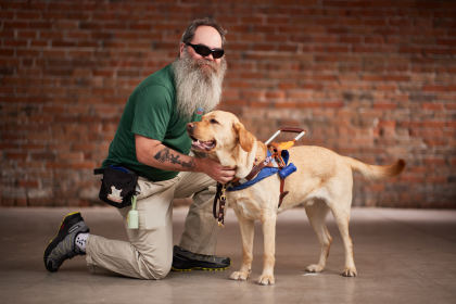 Rob kneeling next to his Yellow Labrador guide dog, Kent