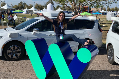 Sandy Karp sits on Waymo Logo in front of a white, Waymo Pacifica in Chandler, Arizona