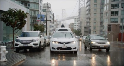 A photo of a white, Waymo Pacifica minivan with its windshield wipers on in rainy San Francisco 