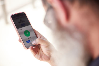 Rob holding a smartphone with a screen that reads "find my car" while his thumb hovers over a button that shows a music symbol