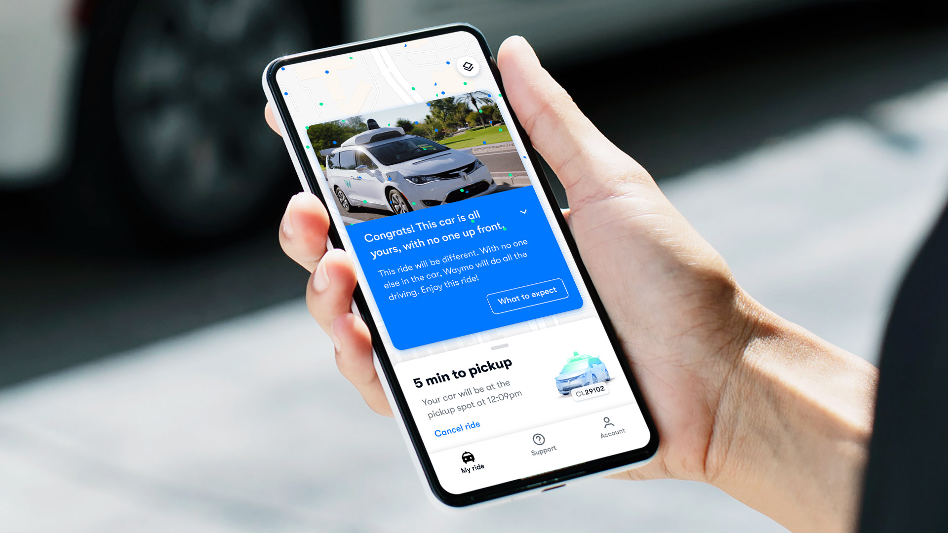 A photo of someone holding a phone and hailing a fully autonomous Waymo One car from the app