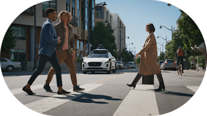 Pedestrians at busy crosswalk with Waymo waiting in the background