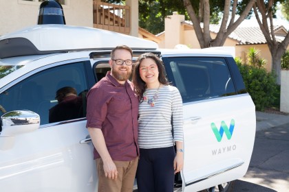 A photo of Amy and Paul in front of a white, Waymo Pacifica minivan 