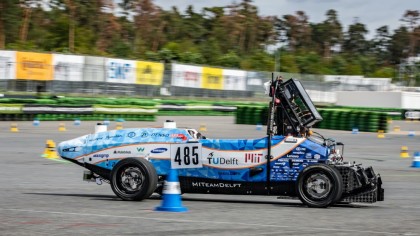 A photo of the blue the MIT/Delft autonomous race car navigating a cone on a race track