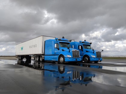 Two, blue Waymo Via trucks on a rainy tarmac 