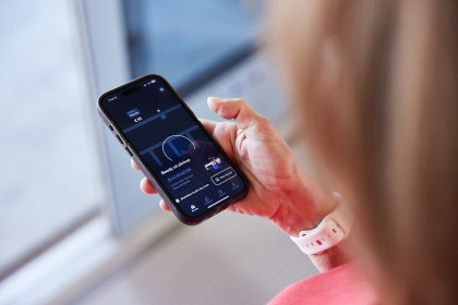 A woman holds an iPhone with the Waymo One app open as her Waymo vehicles arrive at the pickup location