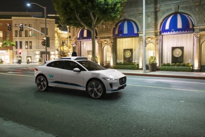 A rendering of a white, I-PACE with the 4th-generation Waymo Driver in an urban setting