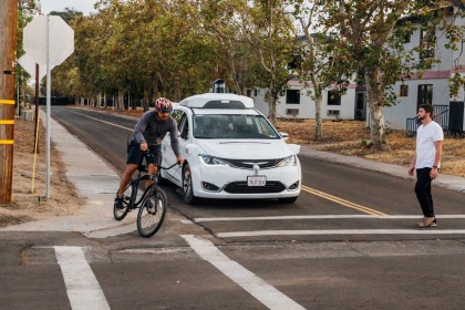 A white, Waymo Pacifica minivan yielding to a pedestrian and cyclist at a closed course testing facility 
