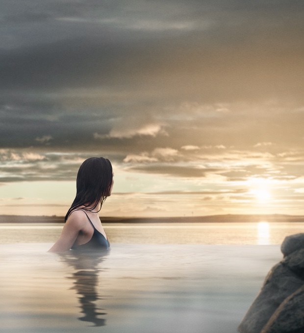 A woman watches the sunset while soaking in the geothermal waters of Sky Lagoon.