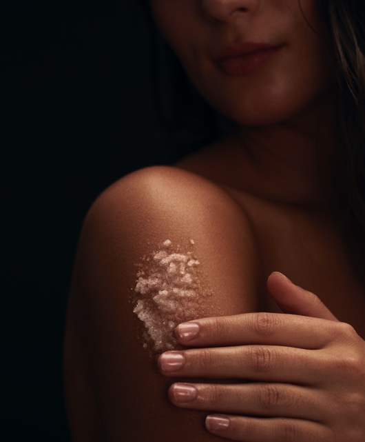 A woman applies the Sky body scrub to her shoulder. 