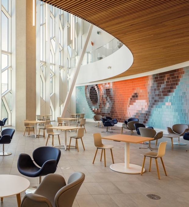The interior of the Calgary Public Library's main branch features tables and comfortable chairs as well as large windows and a colourful wall mosaic.
