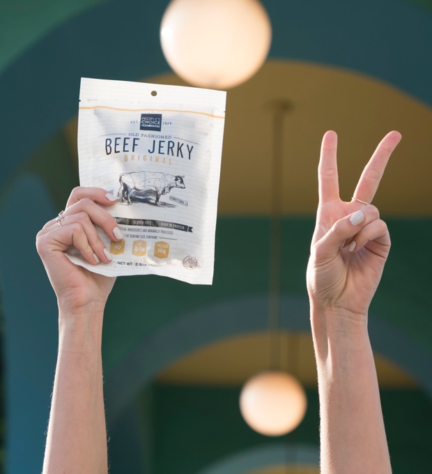A woman holding a bag of People’s Choice beef jerky in one hand while flashing the peace sign with her other hand.
