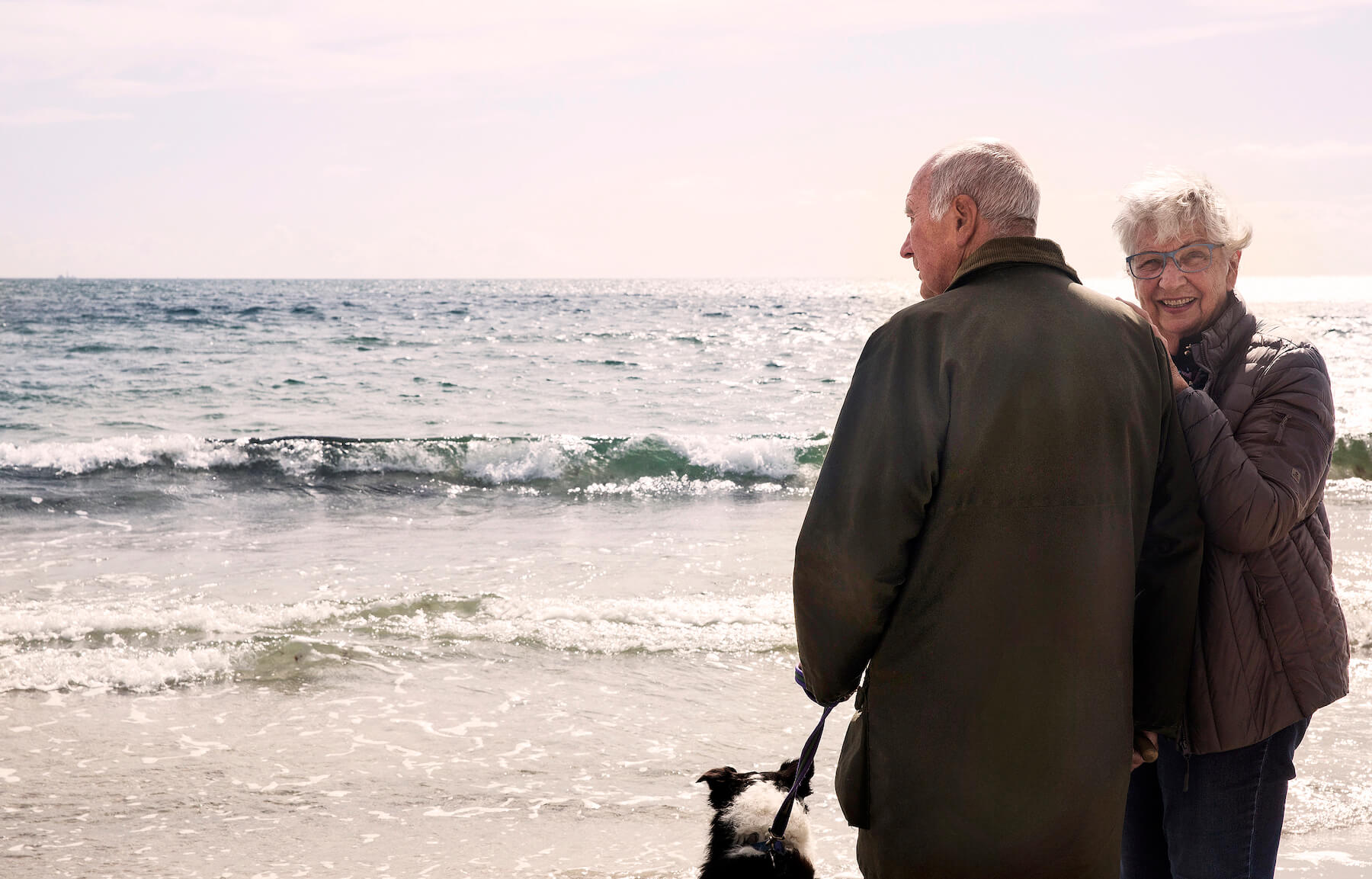 Äldre par med hund på strandpromenad vid havet