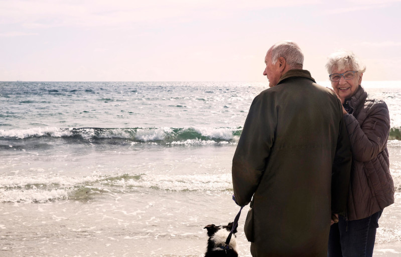 Äldre par med hund på strandpromenad vid havet