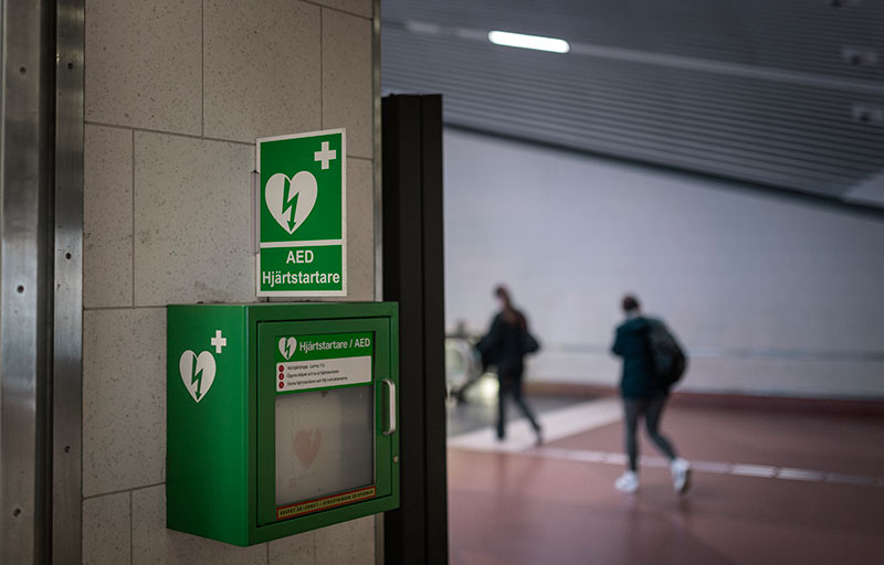 Hjärtstartare på en stenvägg med två människor i förbifarten.