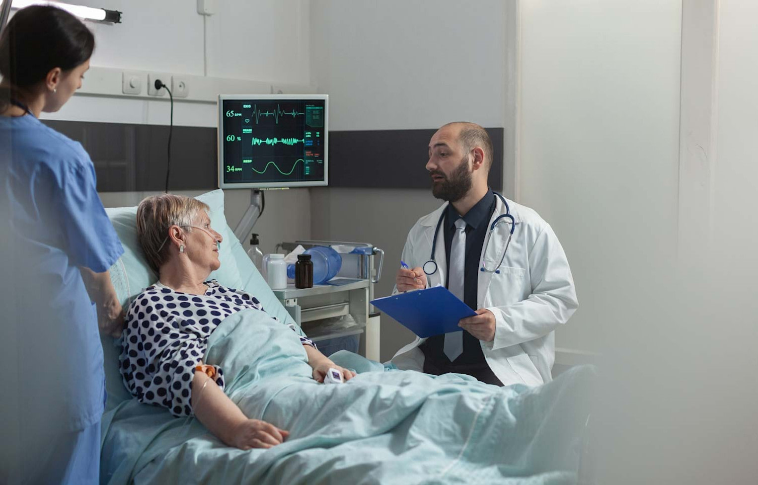 Patient ligger i sjukhussäng och två läkare står bredvid