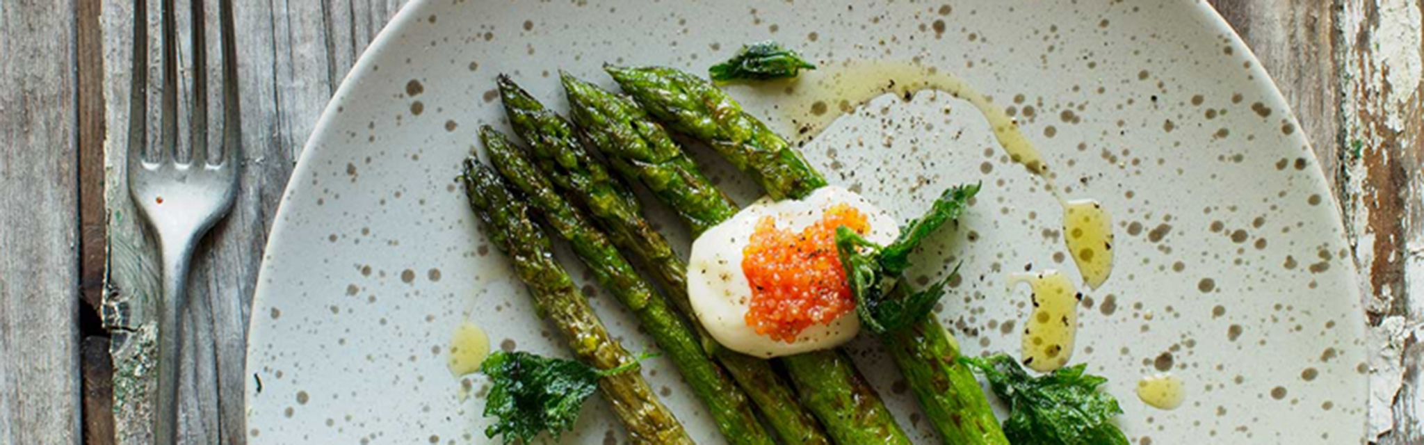 Sparris med snabbstekta nässlor på ett träbord, med en gaffel till vänster.