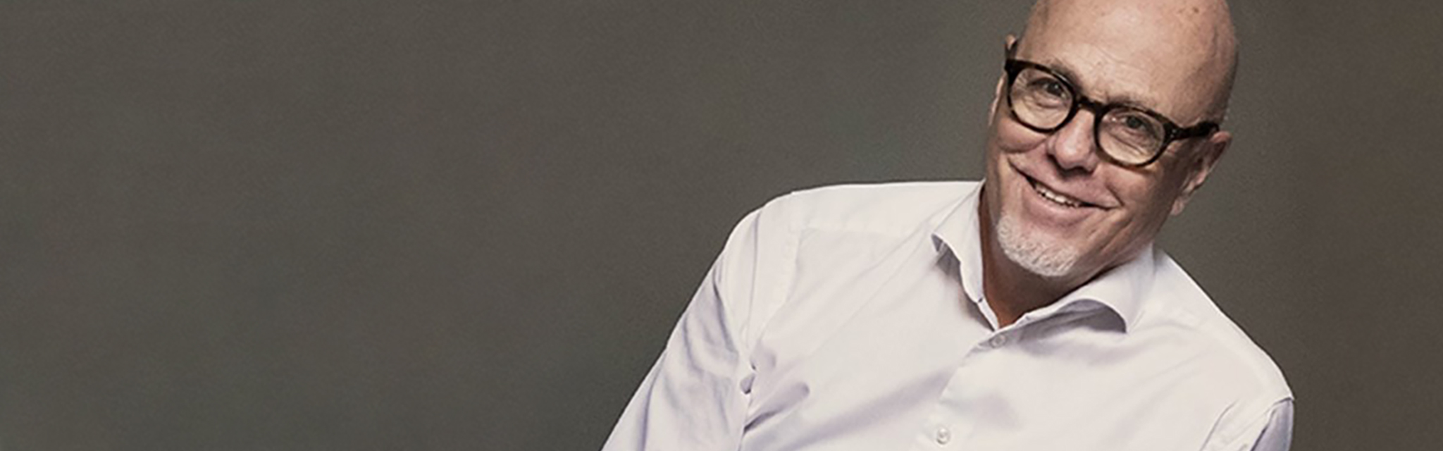 Man i glasögon och vit skjorta mot grå bakgrund.