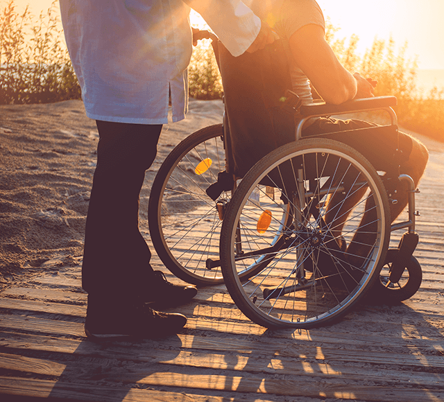 Person i rullstol och anhörig på strand i solnedgång
