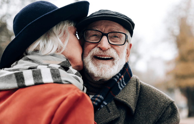 Äldre kvinna pussar en äldre man på kinden
