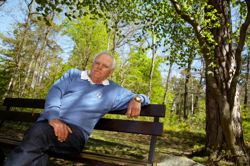 Man i blå tröja sitter på en parkbänk i grönska