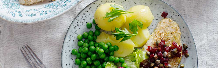 Tallrik med kokt potatis och torsk tillsammans med ärter. På en vit duk.