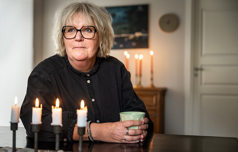 Helena Efraimsson sitter vid ett bord med en grön kopp i händerna. Stearinljus är tända framför och bakom henne.