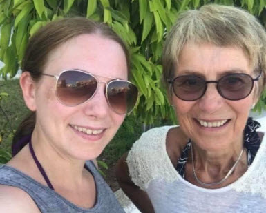 Äldre och yngre kvinna med solglasögon framför grön växt